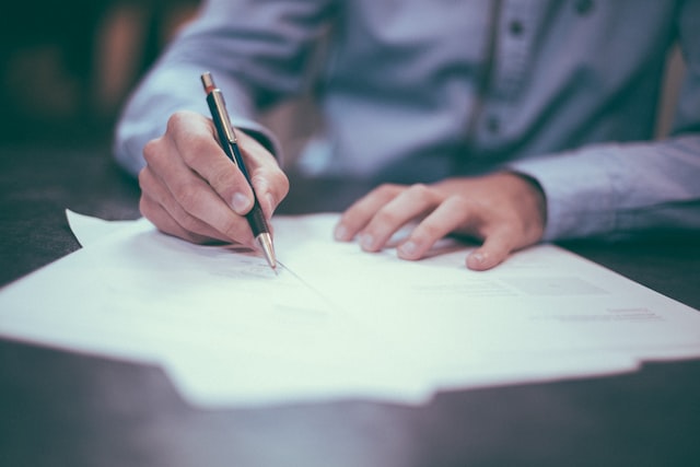 hand signing a document with a black pen