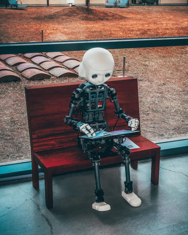 Black and white robot toy sitting on a red bench reading a book