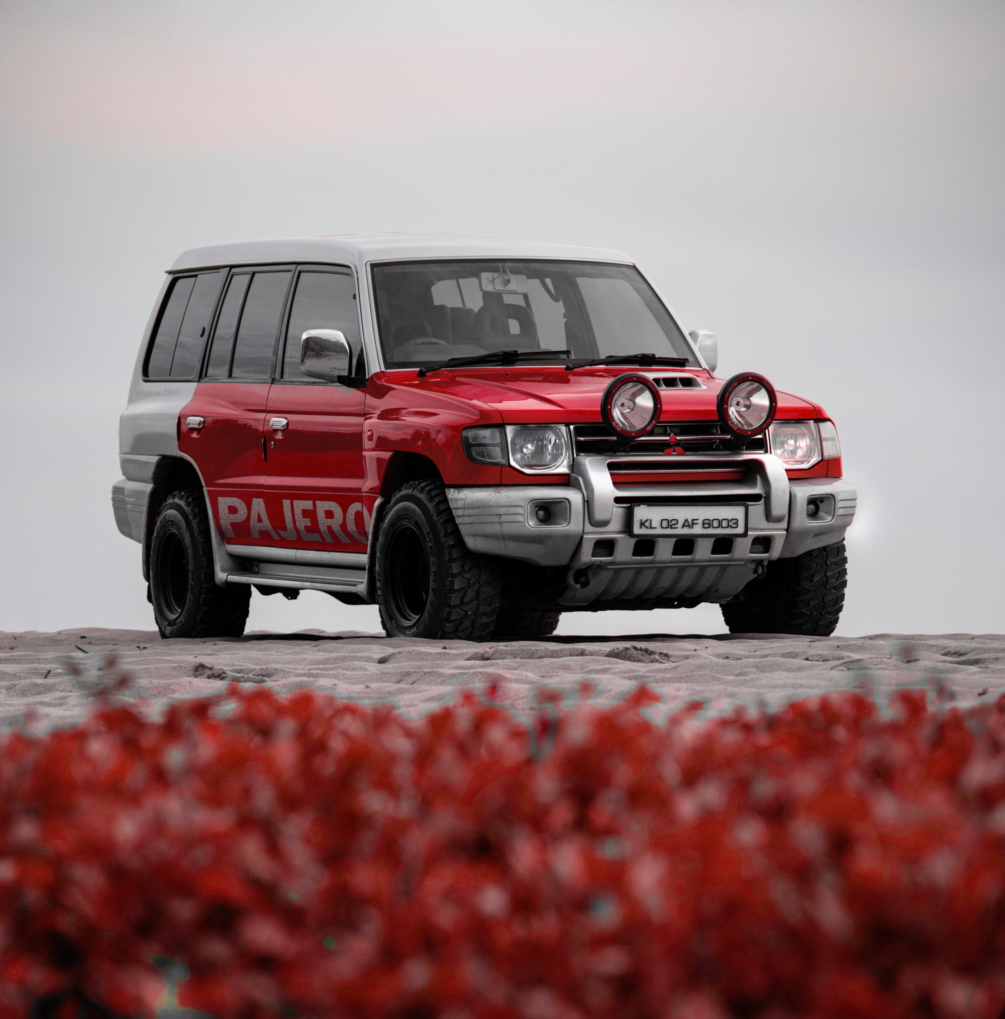 Red and white jeep wrangler on gray sand
