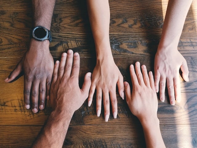 five human hands on a brown surface