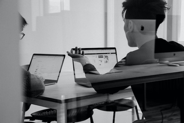 Two people talking in front of computer screens